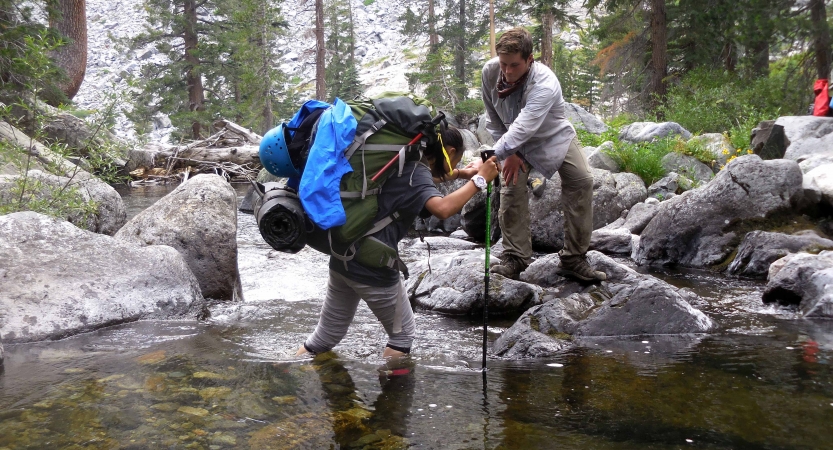 One person helps guide another through knee-deep water. 